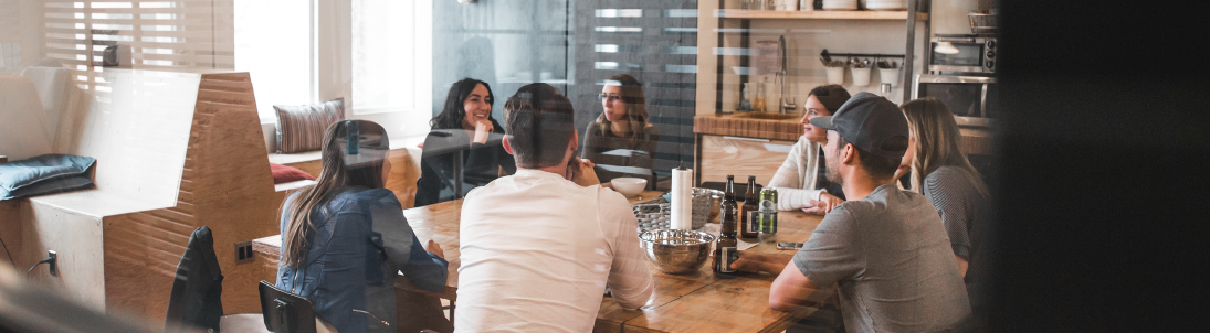 A group of millennial friends sit at a wood table in a restaurant.